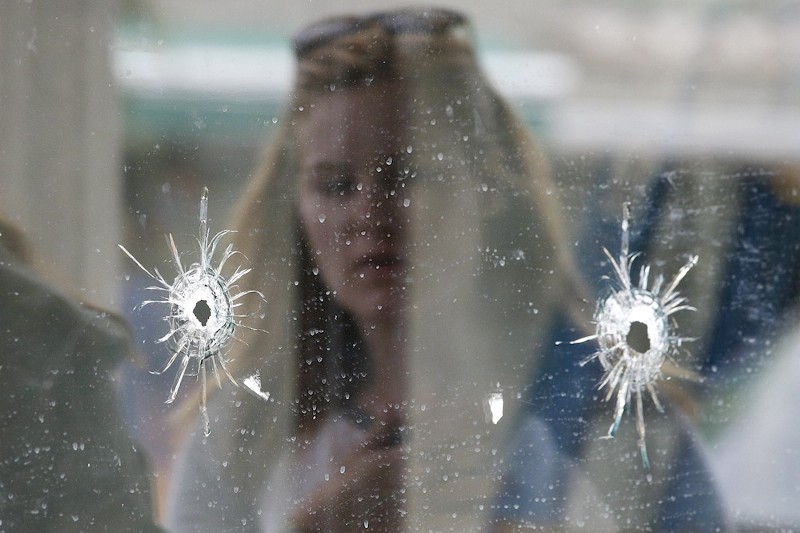 A woman looks at bullet holes on the window of IV Deli Mark, where Friday’s shooting took place CREDIT: AP/JAE C. HONG