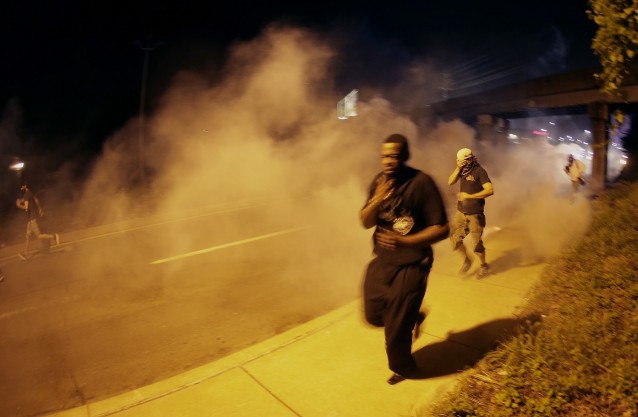 People run from tear gas after police dispersed protesters in Ferguson on Sunday night CREDIT: AP Photo/Charlie Riedel