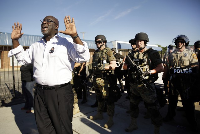 A community activist tries to persuade a group of protesters to move back as police in riot gear watch protesters. CREDIT: AP Photo/Jeff Roberson