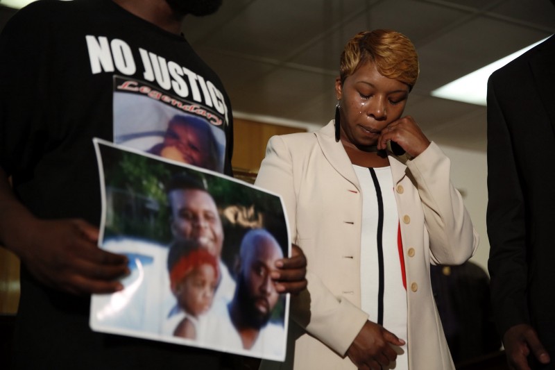 Lesley McSpadden, the mother of 18-year-old Michael Brown, wipes away tears as Brown’s father, Michael Brown Sr., holds up a family picture of himself, his son, top left, and a young child during a news conference Monday, Aug. 11. CREDIT: AP PHOTO/JEFF ROBERSON