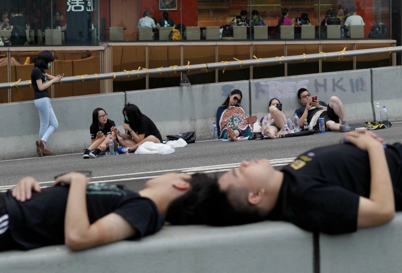 Pro-democracy student protesters in Hong Kong sleep and use their cellphones on a main street outside of the government complex. CREDIT: AP PHOTO/WALLY SANTANA