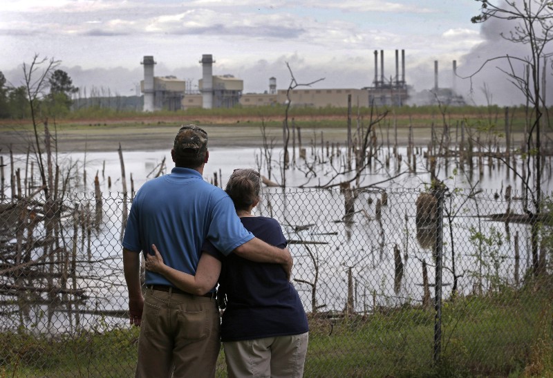 In this April 25, 2014 photo, Bryant Gobble, left, hugs his wife, Sherry Gobble, right, as they look from their yard across an ash pond full of dead trees toward Duke Energy’s Buck Steam Station in Dukeville, N.C. CREDIT: AP PHOTO/CHUCK BURTON