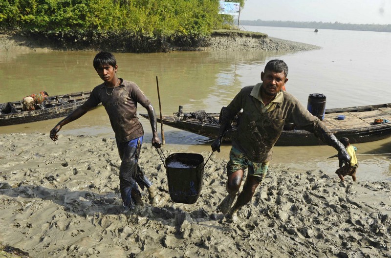 Villagers carry oil in a barrel after removing it from the river surface, after an oil tanker sank in one of the world’s largest mangrove forests in the Sundarbans, in Joymani village, Bangladesh, Saturday, Dec. 13, 2014. The oil tanker carrying more than 350,000 liters (92,500 gallons) of bunker oil sank Tuesday on the major river flowing through the Sundarbans after being hit by a cargo vessel. The slick had spread over up to 70 kilometers (45 miles) of the Shela river, threatening several types of animals including rare Irrawaddy dolphins, a senior official of the Bangladesh Forest Department said. CREDIT: AP PHOTO