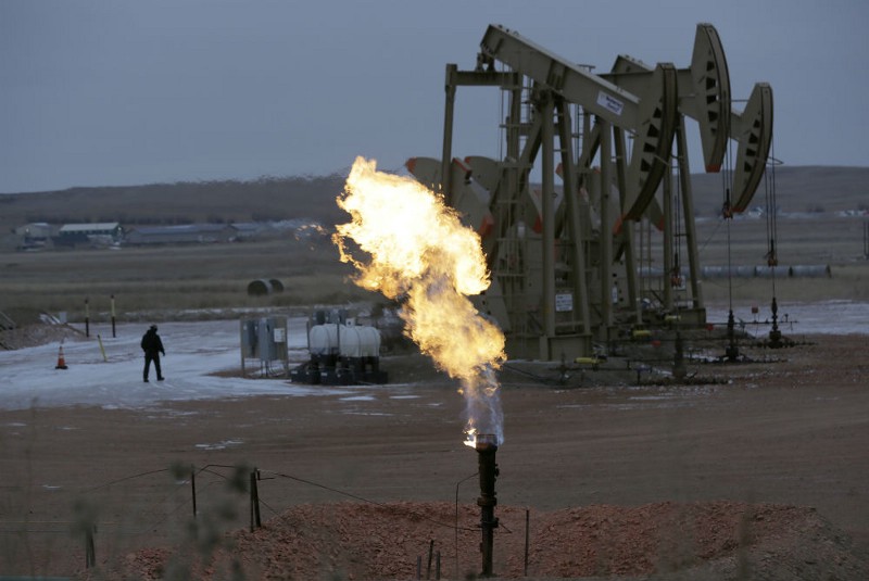 Workers tend to oil pump jacks behind a natural gas flare, Wednesday, Dec. 17, 2014, near Watford City, N.D. CREDIT: AP PHOTO/ERIC GAY