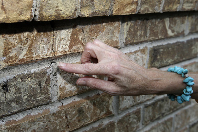 This photo shows Texas resident Barbara Brown pointing to a one of several cracks on an exterior wall of her home, Saturday, June 21, 2014, in Reno. CREDIT: AP PHOTO/TONY GUTIERREZ