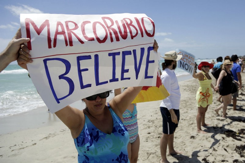 This May 17, 2014, file photo shows Blanca Mesa of Miami protesting against Sen. Marco Rubio’s statements on climate change as activists and beach-goers join hands in a Hands across the Sand demonstration in Miami Beach, Fla. CREDIT: AP PHOTO/LYNNE SLADKY, FILE