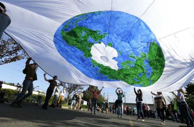 Protesters lift up a circular tarp painted in earth colors during a rally at Terminal 5 at the Port of Seattle, Monday, May 18, 2015, in Seattle where the Polar Pioneer oil drilling rig and other equipment to be used by Royal Dutch Shell for Arctic oil drilling is currently stationed. CREDIT: AP Photo/Ted S. Warren