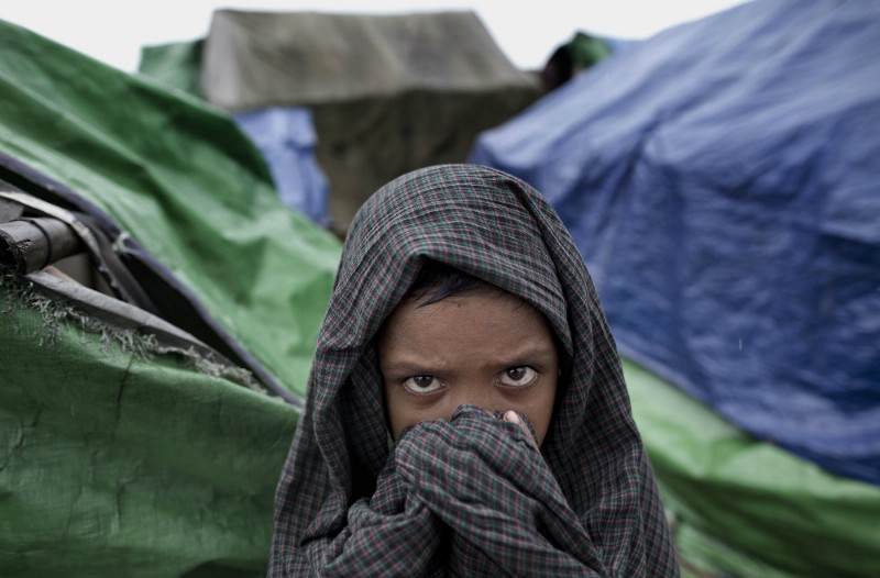 A Rohingya child covers his head and face with a cloth as he stands in the foreground of makeshift tents at Dar Paing refugee camp in north of Sittwe, Rakhine state, Myanmar. CREDIT: AP