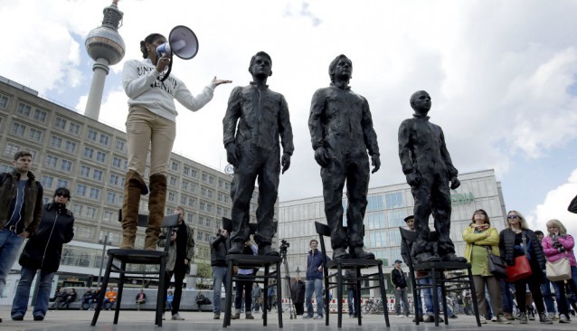 A women delivers a speech as she stands on a chair of the public art project “Anything to Say?” at the Alexander Square in Berlin, Germany, Friday, May 1, 2015. The sculpture of the Italian artist Davide Dormino shows the whistleblowers Chelsea Manning, Julian Assange and Edward Snowden, from right, to honour their courage. CREDIT: AP