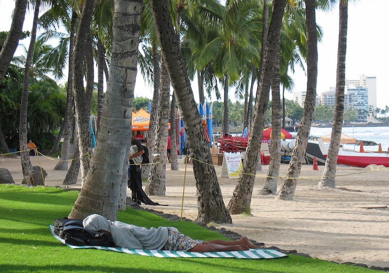 A homeless man sleeps near Waikiki Beach CREDIT: AP/CATHY BUSSEWITZ