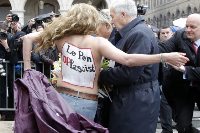 FEMEN activist with “Le Pen Top Fascist” painted on her body appears as Frances far-right National Front president Marine Le Pen places a wreath at Joan of Arc statue during its annual May Day march, in Paris, France, Friday, May 1, 2015. CREDIT: AP