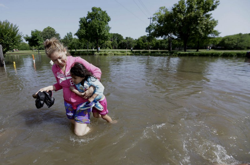 Nayeli Cervantes carries her friend’s daughter Sophia Aviles through the floodwaters outside their apartment in Houston, Tuesday, May 26, 2015. Heavy rain overnight cause some major highways to be closed in the Houston area. CREDIT: AP PHOTO/DAVID J. PHILLIP