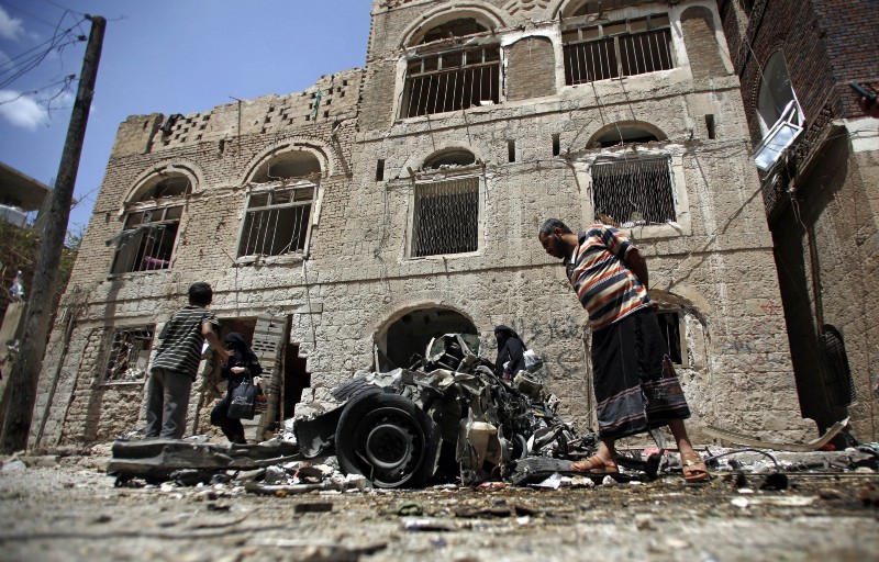 People stand amid wreckage of a vehicle at the site of a car bomb attack in Sanaa, Yemen, Tuesday, June 30, 2015. CREDIT: AP