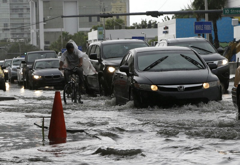 A cyclist and vehicles negotiate heavily flooded streets as rain falls, Tuesday, Sept. 23, 2014, in Miami Beach, Fla. CREDIT: AP PHOTO/LYNNE SLADKY
