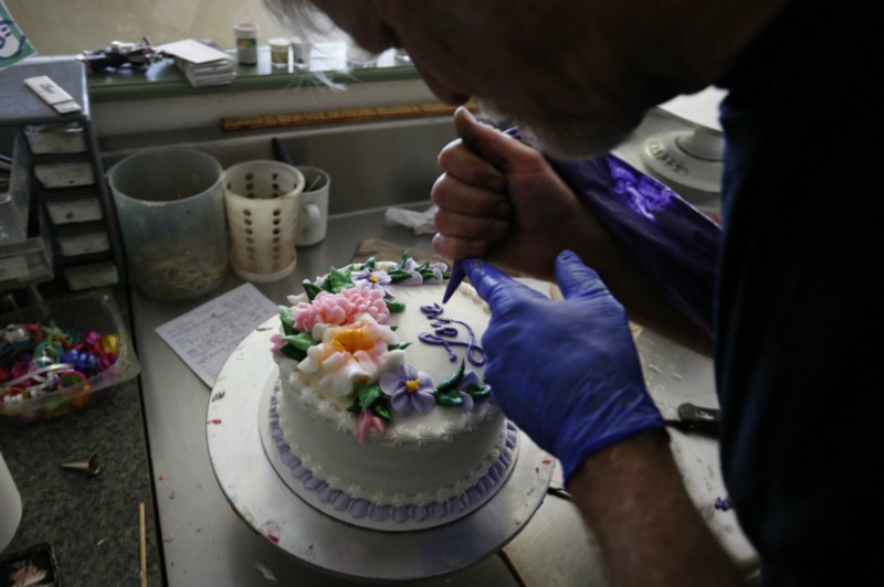 Jack Phillips decorating a cake with the word, “Love.” CREDIT: AP PHOTO/BRENNAN LINSLEY