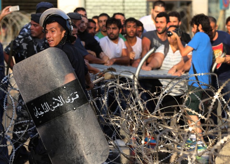 A Lebanese riot policeman, foreground, reacts, as activists, background, remove barriers as they try to cross to the government house, during a protest against the ongoing trash crisis, in downtown Beirut. CREDIT: AP Photo/Hussein Malla
