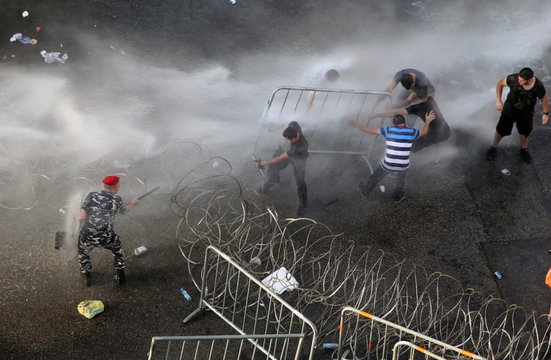 Lebanese activists, right, remove barriers as they try to cross to the government house, as riot police spray them with water cannons during a protest against the ongoing trash crisis. CREDIT: AP Photo/Bilal Hussein