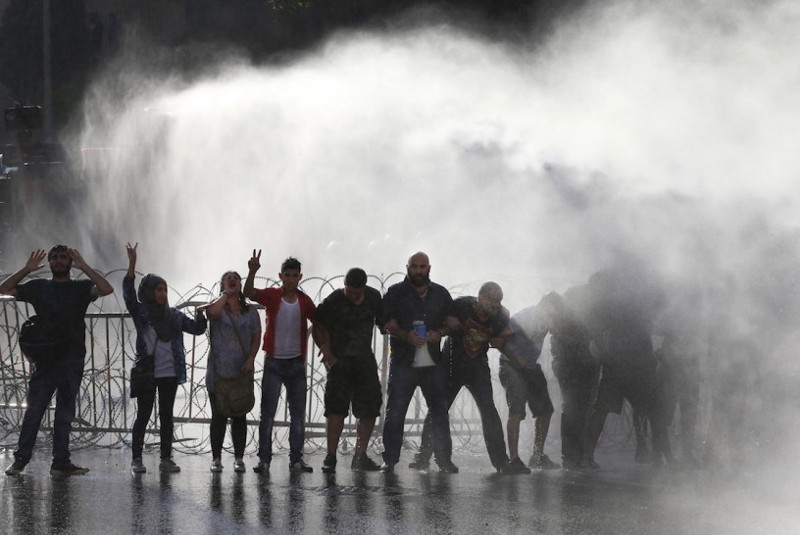 Lebanese activists shout anti-government slogans as they are sprayed by riot police using water cannons. CREDIT: AP Photo/Hussein Malla
