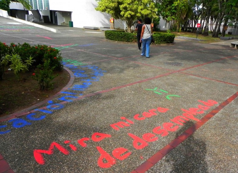 Student Coraly León walks by graffiti that reads, “Look into my unemployed face.” CREDIT: Alice Ollstein