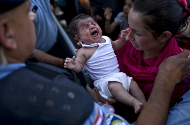 A woman carries a baby as she goes through a police cordon in Tovarnik, Croatia, Thursday, Sept. 17, 2015. CREDIT: AP Photo/Marko Drobnjakovic