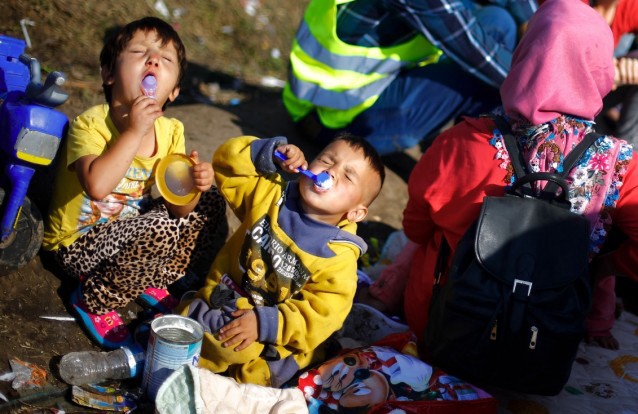 Young children eat milk powder as they wait for a bus in a temporary holding center for migrants near the border between Serbia and Hungary in Roszke, southern Hungary, Sunday, Sept. 13, 2015. CREDIT: AP Photo/Matthias Schrader