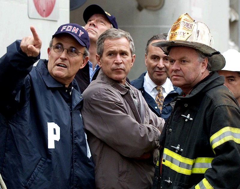 In this Sept. 14, 2001 file photo President George W. Bush, center, with, from left, former New York City Mayor Rudolph Giuliani, then-New York Gov. George Pataki, Sen. Charles Schumer, D-N.Y., and former New York City Fire Commissioner Thomas Van Essen look toward the fallen buildings during a tour of the World Trade Center. CREDIT: AP PHOTO/DOUG MILLS, FILE