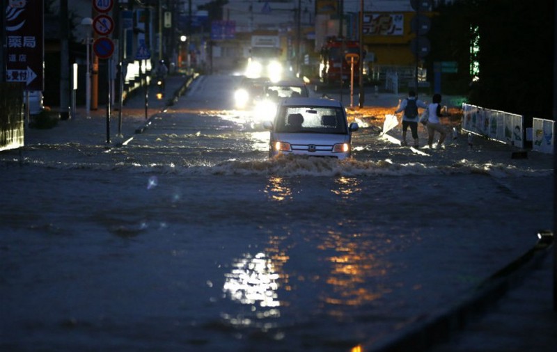 Vehicles drive through a flooded street in Joso, Ibaraki prefecture, north of Tokyo, Thursday, Sept. 10, 2015. Raging floodwaters broke through a flood berm Thursday and swamped the city north of Tokyo, washing away houses, forcing dozens of people to rooftops to await helicopter rescues. CREDIT: AP Photo/Shizuo Kambayashi