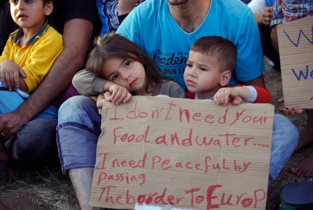 In this photo taken late Wednesday, Sept 16, 2015, a man show a placard as migrants, mostly Syrians, trying to reach Europe rest outside the Turkish city of Edirne, which borders European Union members Greece and Bulgaria. CREDIT: AP Photo/Emrah Gurel