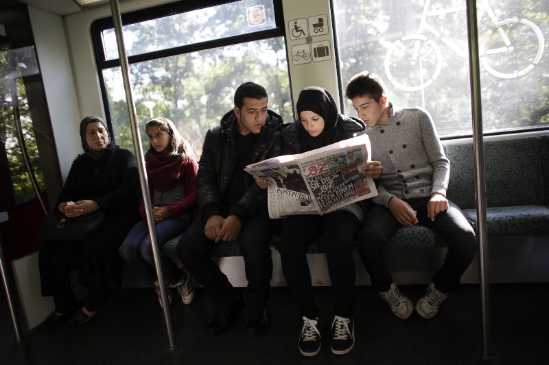 In this photo taken on Wednesday, Sept. 9, 2015, Syrian refugee family, Reem Habashieh, second from right, and her brothers Yaman Habashieh, right, and Mohammed Habashieh, center, sit in a train and read in that day’s edition of the local news paper BZ with special pages in Arabic for refugees CREDIT: AP PHOTO/MARKUS SCHREIBER