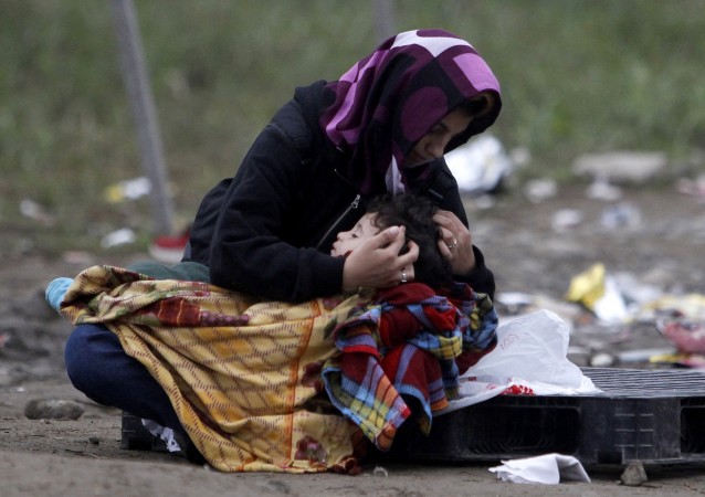 A woman tries to keep her child warm while waiting to enter the transit camp for refugees near the southern Macedonian town of Gevgelija, after crossing the border from Greece, early Friday, Oct. 16, 2015. CREDIT: AP Photo/Boris Grdanoski