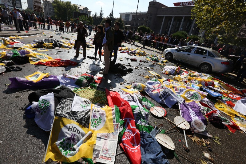 People surround the area where bodies of victims are covered with flags and banners at the site of an explosion in Ankara, Turkey, Saturday, Oct. 10, 2015. Two bomb explosions apparently targeting a peace rally in Turkey’s capital Ankara on Saturday has killed over a dozen people, a news agency and witnesses said. The explosions occurred minutes apart near Ankara’s train station as people gathered for the rally organized by the country’s public sector workers’ trade union. CREDIT: AP PHOTO/BURHAN OZBILICI