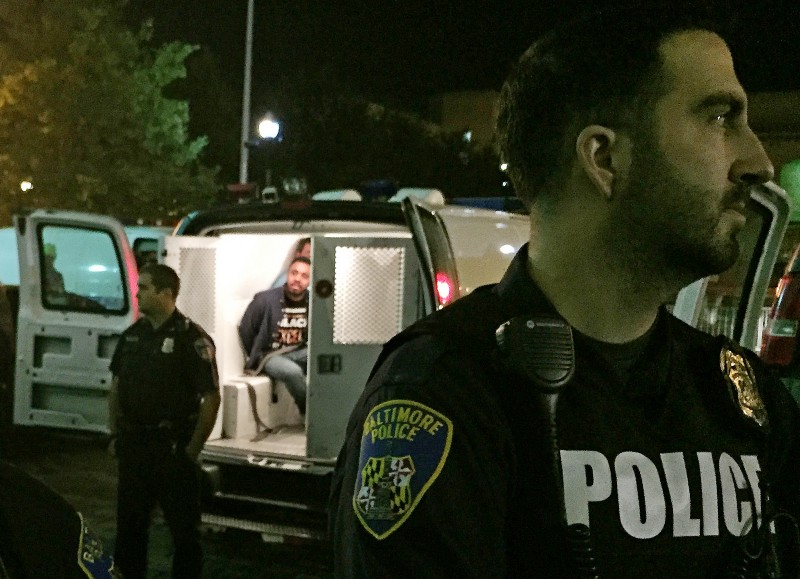 Police stand near vans holding protesters early Thursday, Oct. 15, 2015, in Baltimore. The Baltimore Uprising coalition had occupied City Council chambers at city hall to pretest a council subcommittee’s vote in favor of making the interim police commissioner permanent. CREDIT: AP PHOTO/JULIET LINDERMAN