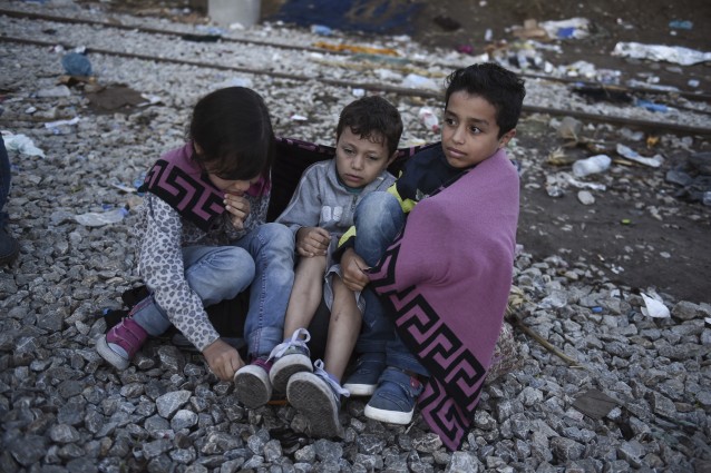 Syrian children try to keep warm as they wait with their families to cross the borde from the northern Greek village of Idomeni to southern Macedonia, Saturday, Sept. 12, 2015. CREDIT: AP Photo/Giannis Papanikos