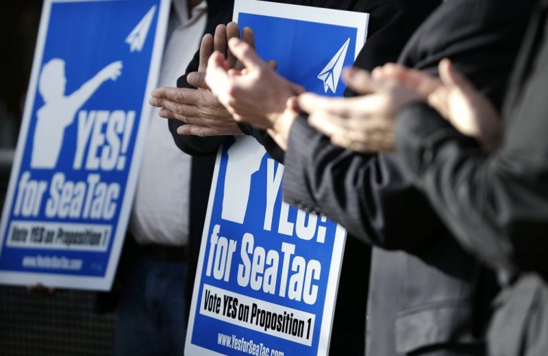 Supporters of a $15 minimum wage applaud behind a speaker at Seattle-Tacoma International Airport during a news conference Tuesday, Nov. 26, 2013, in Seattle. CREDIT: AP Photo/Elaine Thompson