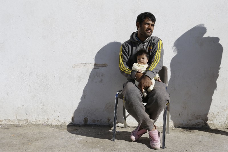 An Afghan migrant holds his baby at Galatsi Olympic Hall in Athens CREDIT: AP PHOTO/THANASSIS STAVRAKIS