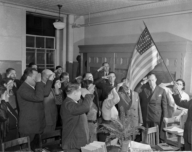 Refugees from Europe salute the U.S. flag as they study for citizenship examinations in New York, Nov. 22, 1938. Thousands have applied for admittance to the country in recent weeks. (AP Photo/John Lindsay) CREDIT: AP PHOTO/JOHN LINDSAY