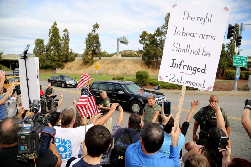 Demonstrators watch as President Barack Obama’s motorcade leaves Roseburg High School after a visit with families of victims of the shootings at Umpqua Community College in Roseburg, Ore., Friday, Oct. 9, 2015. The protesters were angry about Obamas calls for gun restrictions in the wake of the shooting rampage that killed eight students and a teacher at the college. CREDIT: AP PHOTO/RYAN KANG