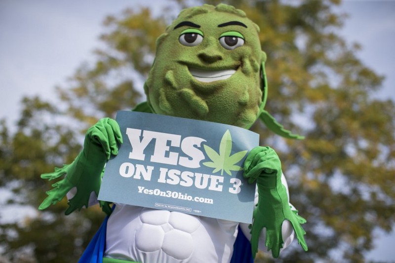 Buddie, the mascot for the pro-marijuana legalization group ResponsibleOhio, holds a sign during a promotional tour stop at Miami University, Friday, Oct. 23, 2015, in Oxford, Ohio. CREDIT: AP Photo/John Minchillo