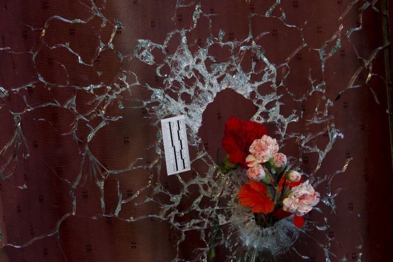 Flowers are put in a window shattered by a bullet as a forensic marker sits next to the impact as people pay their respect to the victims at the site of the attacks on restaurant Le Petit Cambodge in Paris, France on Sunday, Nov. 15, 2015. CREDIT: AP PHOTO/PETER DEJONG