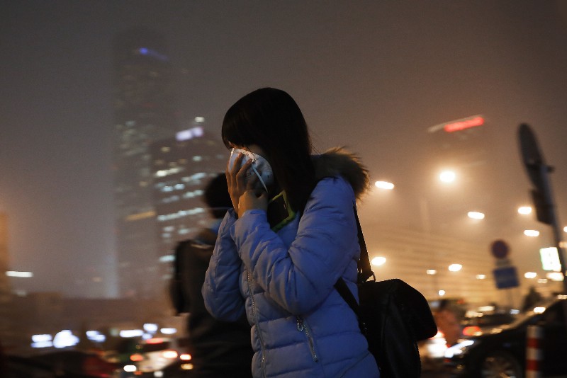 A woman covers her face with a mask as she rushes to a subway station on a heavily polluted day in Beijing Tuesday, Dec. 8, 2015. (AP Photo/Andy Wong)