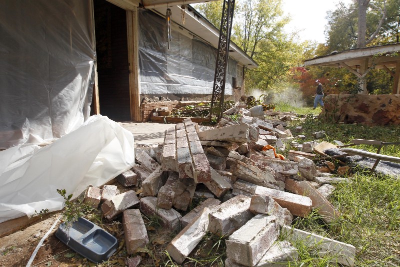 Chad Devereaux works to clear up bricks that fell from three sides of his in-laws’ home in Sparks, Okla, after two earthquakes hit the area in less than 24 hours. Oil and gas companies say the industry can’t survive if they are held accountable for earthquake damage. CREDIT: AP PHOTO/SUE OGROCKI