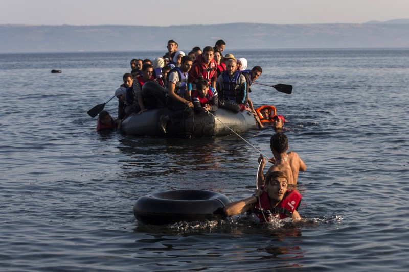 Two migrants pull an overcrowded dinghy with Syrian and Afghan refugees arriving from the Turkish coast to the Greek island of Lesbos. CREDIT: AP PHOTO/SANTI PALACIOS