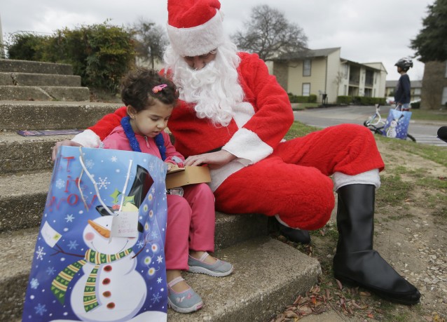 Newly arrived Syrian refugee Jory, 4, left, receives a gift outside her family’s apartment from volunteer Tim Blystone, right, portraying Santa Claus, Saturday, Dec. 12, 2015, in Dallas. Volunteers from the DFW International Community Alliance, the Spanish House and the APCA Asian American Resource Group from AT&T all teamed up to provide refugee children with gifts for their first Christmas in America. (AP Photo/LM Otero) CREDIT: AP Photo/LM Otero