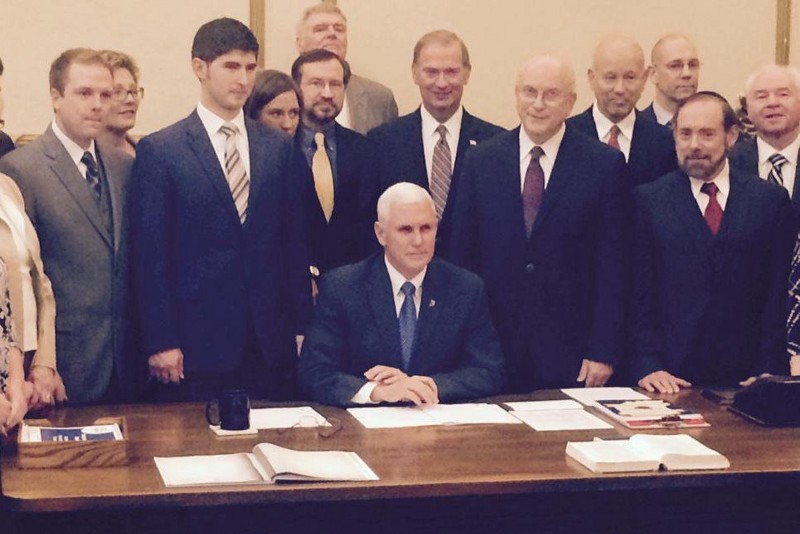 Micah Clark of the American Family Association of Indiana (solid yellow tie) and Curt Smith of the Indiana Family Institute (tall in back) stood behind Gov. Mike Pence (R-IN) as he signed the original Religious Freedom Restoration Act, which had no exemptions for nondiscrimination protections. They helped write that original bill. CREDIT: TWITTER/AMERICAN FAMILY ASSOCIATION OF INDIANA