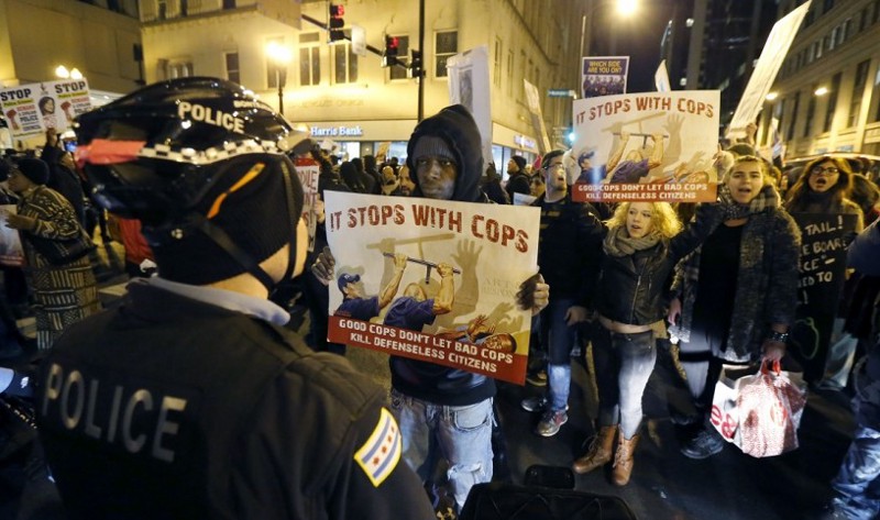 Protester D. lawrence holds a poster in front of a Chicago police officer during a march through Chicago’s Loop calling for Chicago Mayor Rahm Emanuel and Cook County State’s Attorney Anita Alvarez to resign in the wake of a police scandal, Thursday, Dec. 10, 2015. CREDIT: Charles Rex Arbogast, AP