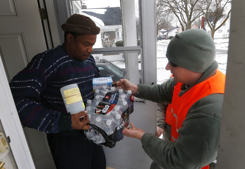 Louis Singleton receives water filters, bottled water and a test kit from Michigan National Guard Specialist Joe Weaver as clean water supplies are distributed to residents, Thursday, Jan. 21, 2016 in Flint, Mich. The National Guard, state employees, local authorities and volunteers have been distributing lead tests, filters and bottled water during the city’s drinking water crisis. (AP Photo/Paul Sancya) CREDIT: AP PHOTO/PAUL SANCYA