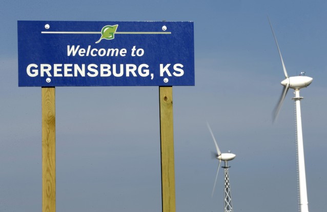Wind turbines rise beyond a sign welcoming visitors to Greensburg, KS. CREDIT: AP Photo/Charlie Riedel
