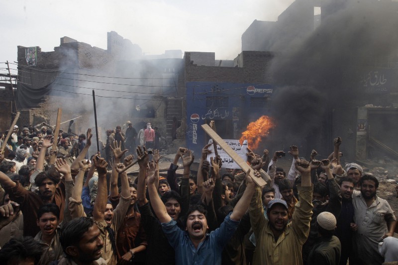 An angry mob reacts after burning Christian houses in Lahore, Pakistan, Saturday, March 9, 2013. A mob of hundreds of people in the eastern Pakistani city of Lahore attacked a Christian neighborhood Saturday and set fire to homes after hearing accusations that a Christian man had committed blasphemy against Islam’s prophet Mohammed, said a police officer. Placard center reads, “ Blasphemer is liable to death.” CREDIT: AP PHOTO/K.M. CHAUDARY