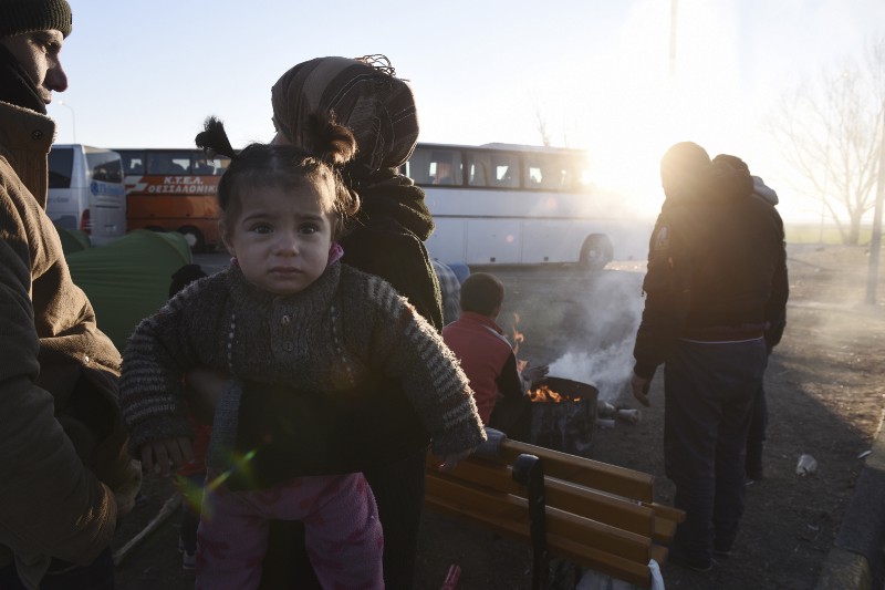 A Syrian woman holds her daughter as refugees try to keep themselves warm around a fire at a parking area near the northern Greek village of Idomeni, on Saturday, Feb. 6, 2016. CREDIT: AP PHOTO/GIANNIS PAPANIKOS