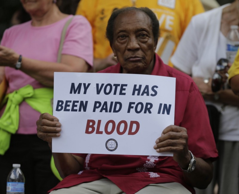 A man holds a protest sign at a rally in Winston-Salem, N.C., Monday, July 13, 2015 after the beginning of a federal voting rights trial challenging a 2013 state law. CREDIT: AP PHOTO/CHUCK BURTON